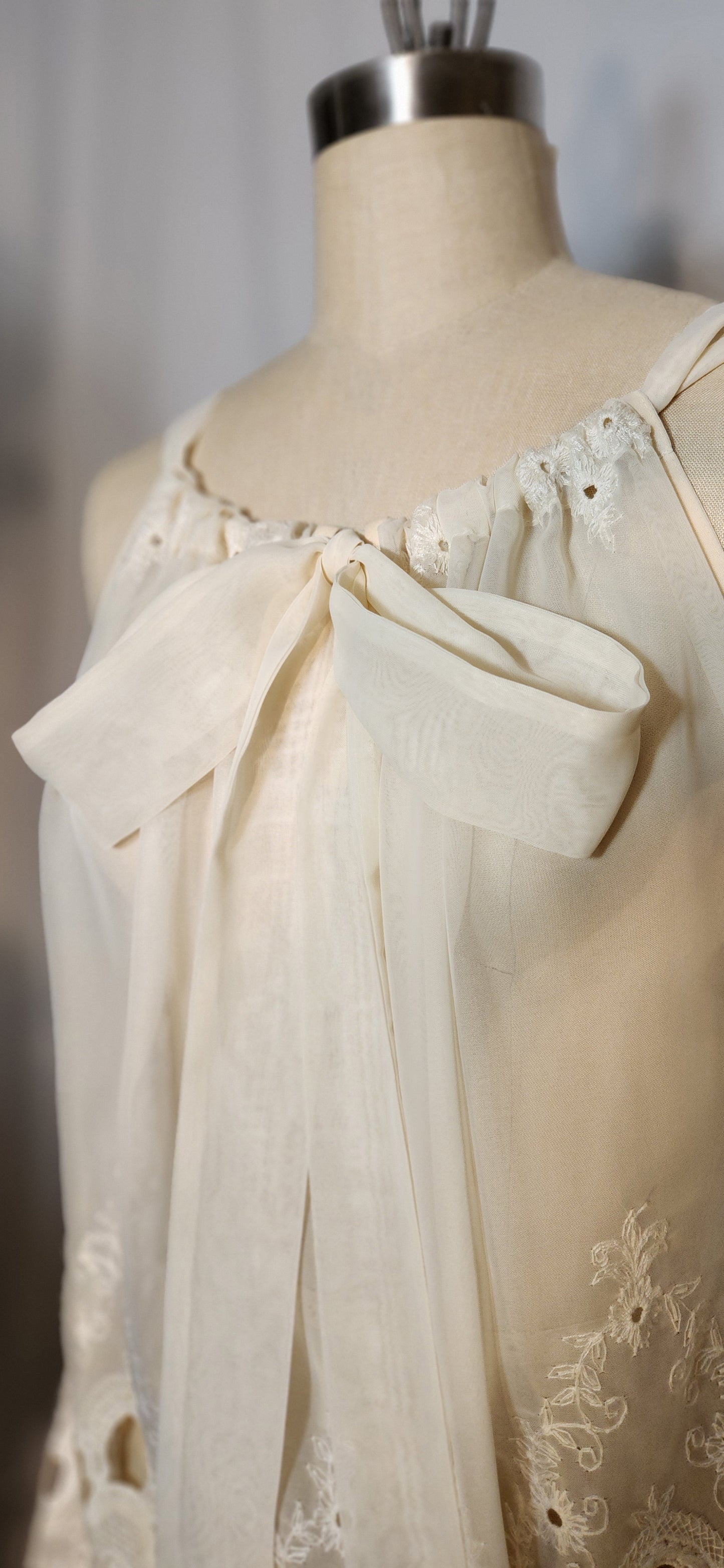 Mannequin wearing a cream-colored dress with lace details and a large bow.