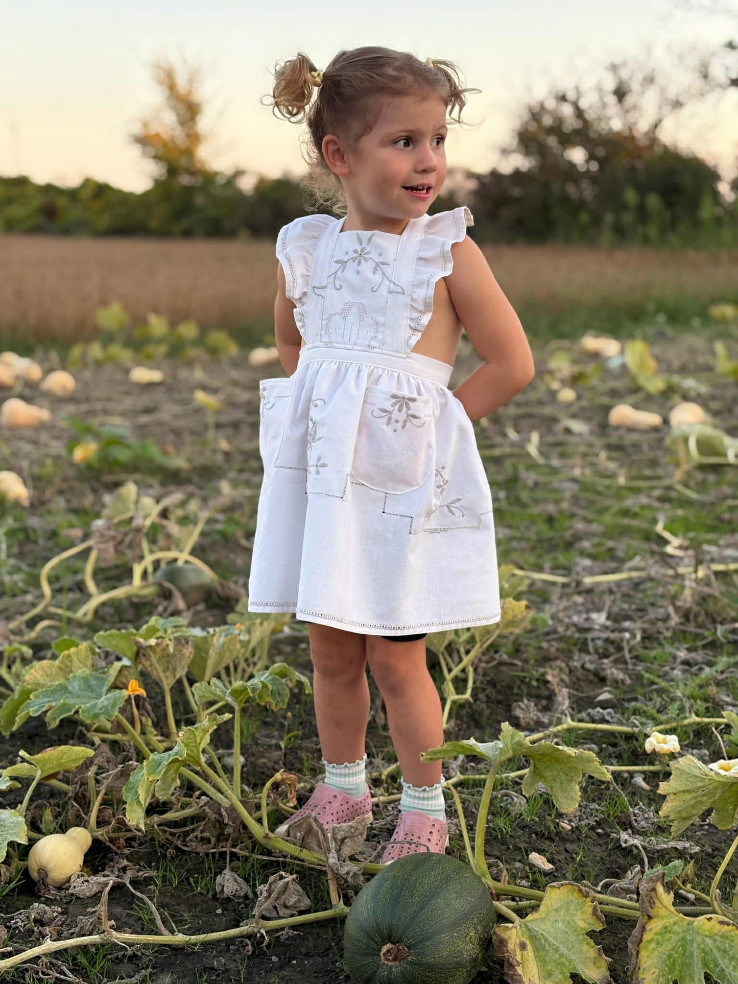 Young girl in a white dress apron standing in a pumpkin patch.