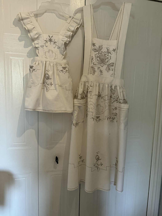Children and adult matching aprons, white with beige embroidery flowers on a white background