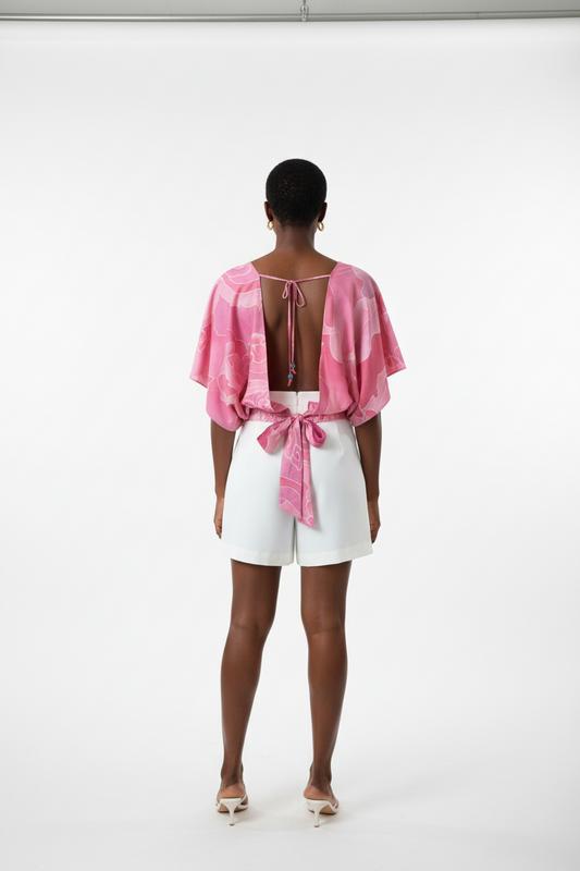 Person wearing a pink open-back top and white shorts on a white background