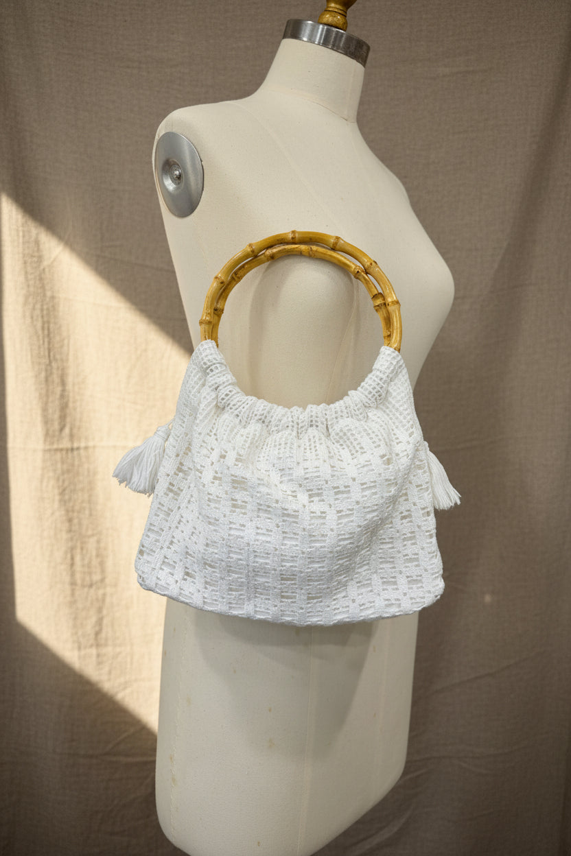 White crochet handbag with a yellow bamboo handle on a mannequin against a brown background