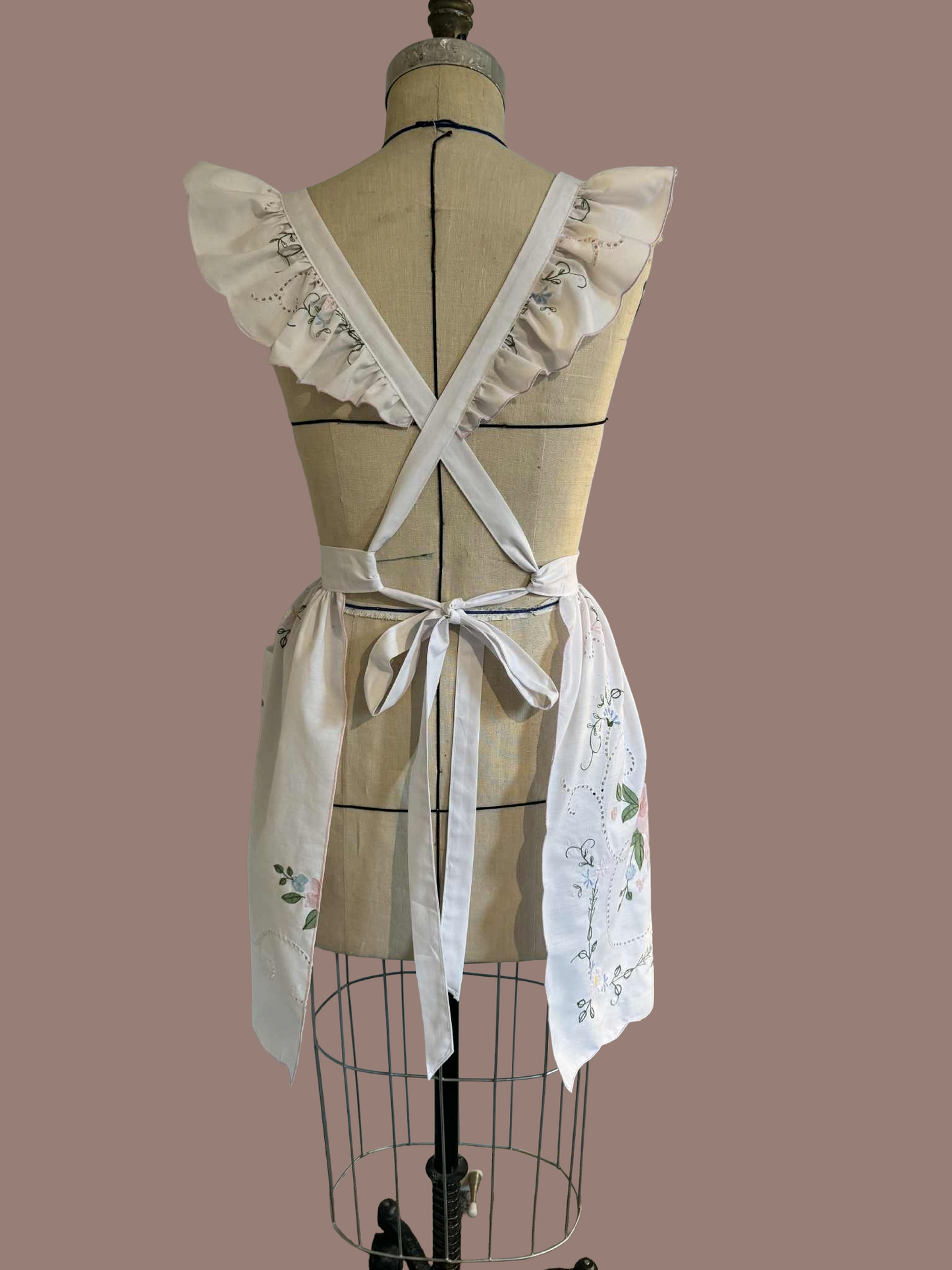 Back view of a white apron with lace details on a mannequin against a brown background