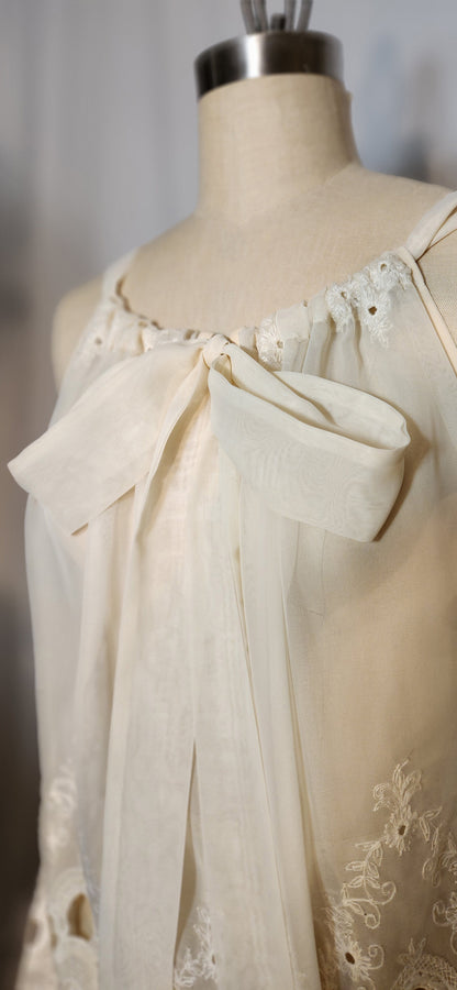 Mannequin wearing a cream-colored dress with lace details and a large bow.