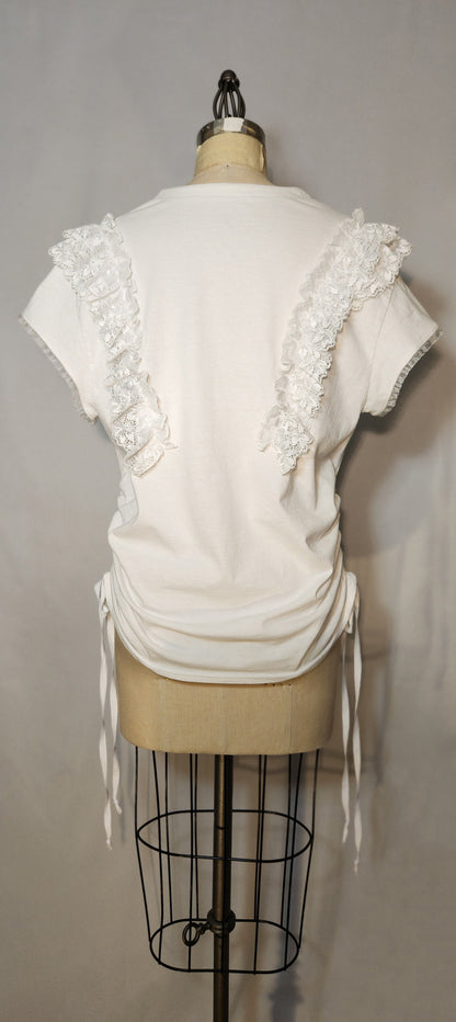 White top with floral embellishments on a mannequin against a gray background