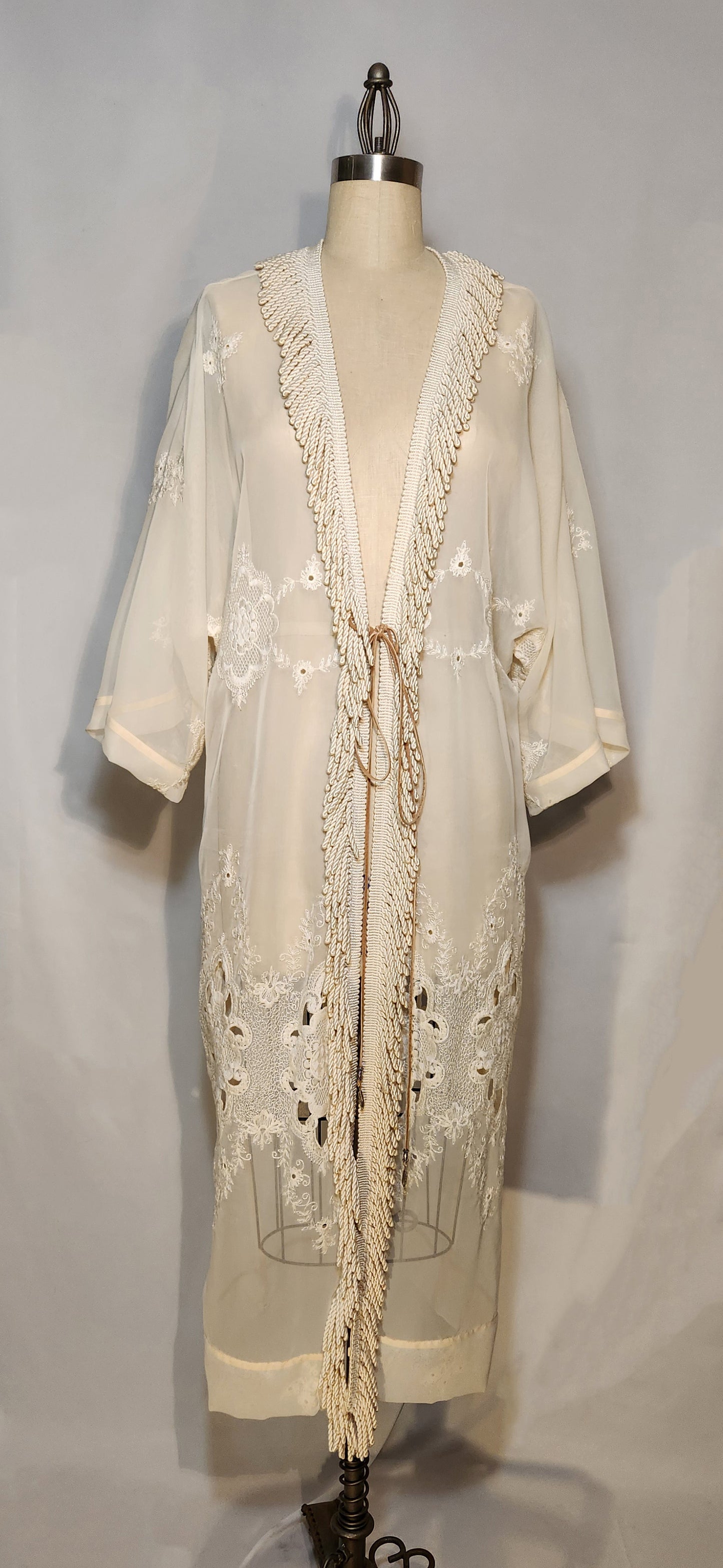 Cream-colored embroidered dress on a mannequin against a gray background