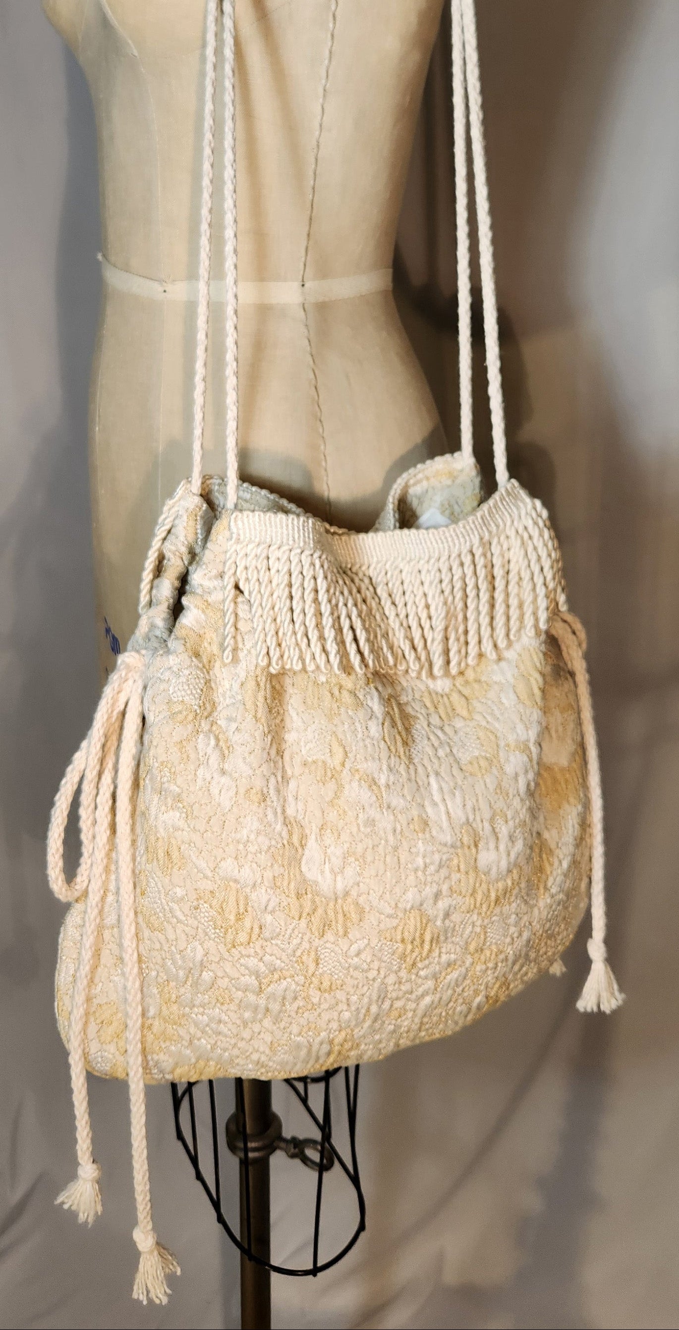 Beige woven handbag on a mannequin against a plain background