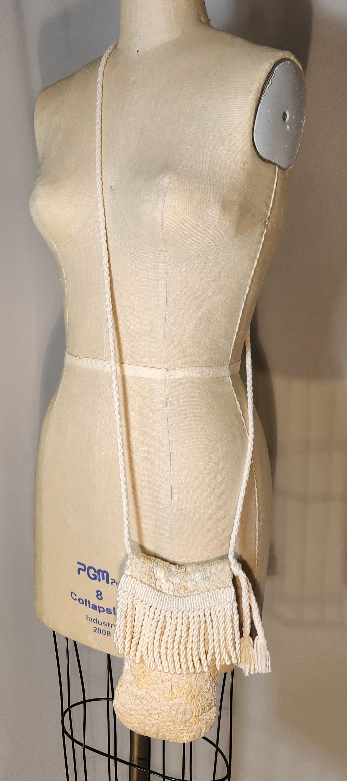 Mannequin wearing a beige garment with fringes on a plain background