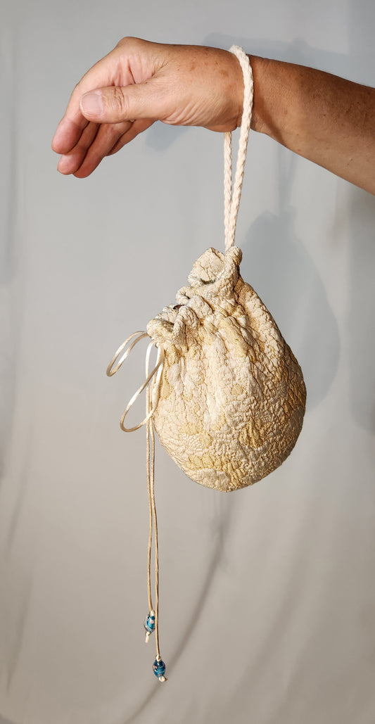 Hand holding a textured beige drawstring bag against a plain background