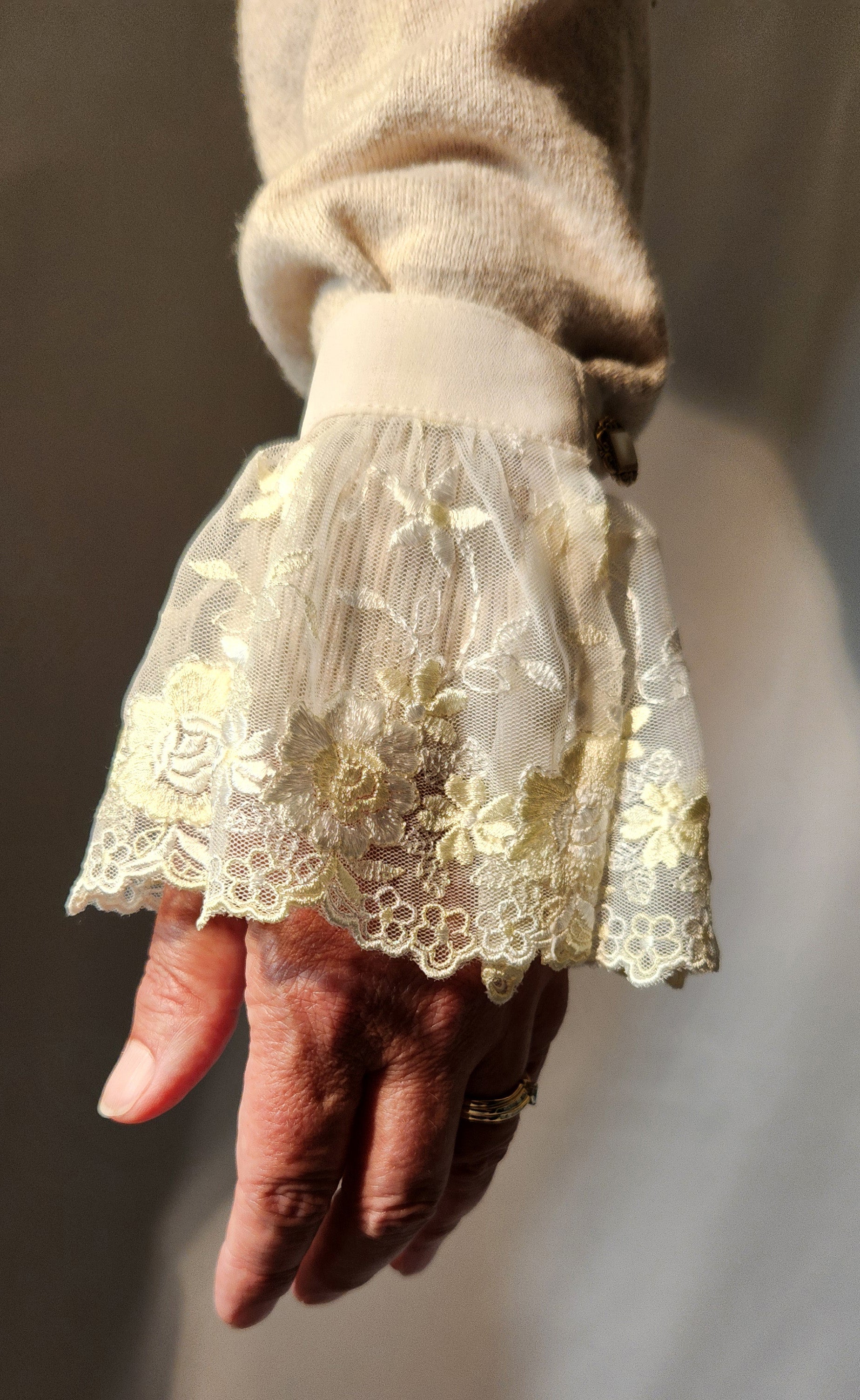 Hand wearing a lace cuffs with a floral pattern against a neutral background