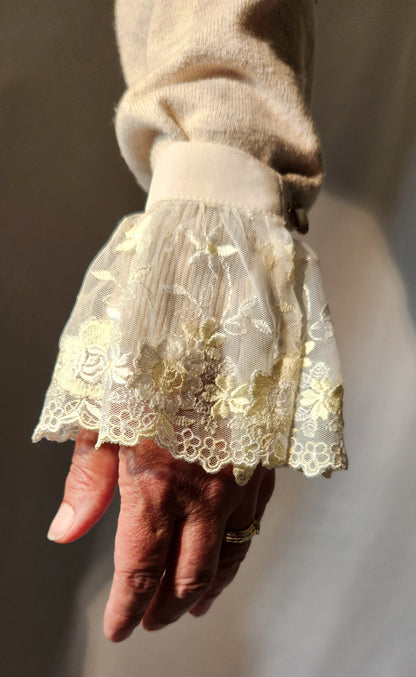 Hand wearing a lace cuffs with a floral pattern against a neutral background