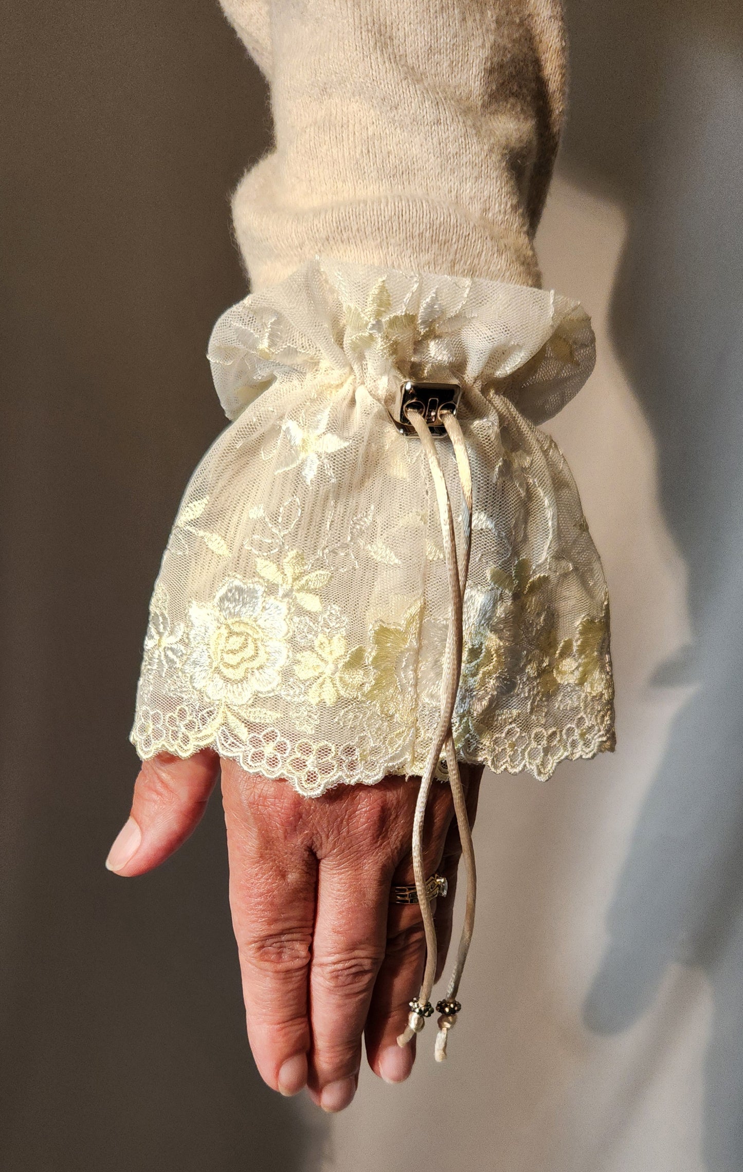 Hand with a lace cuff floral embroidery against a neutral background