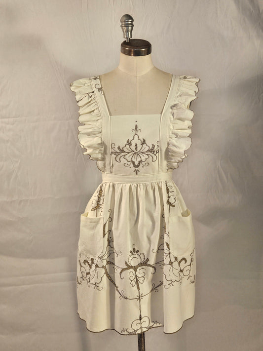 White dress with black floral embroidery on a mannequin against a plain background