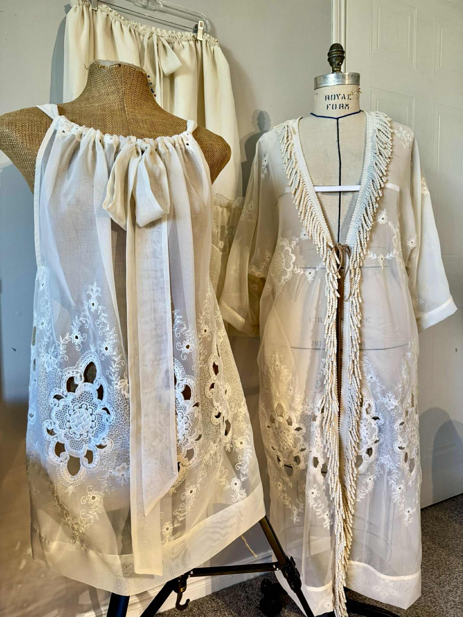 Two mannequins wearing cream-colored lace garments in a room setting.