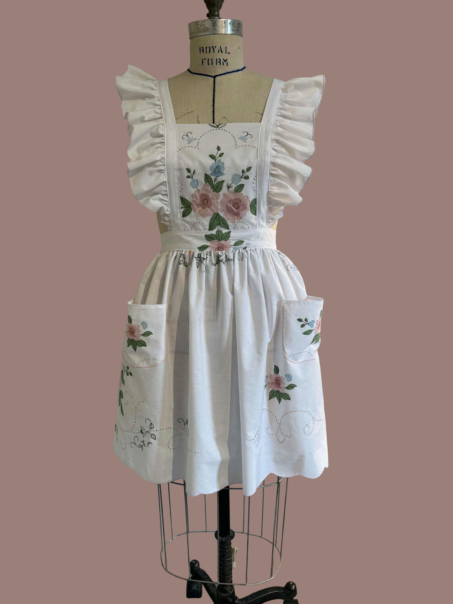 White apron with floral embroidery on a mannequin against a brown background