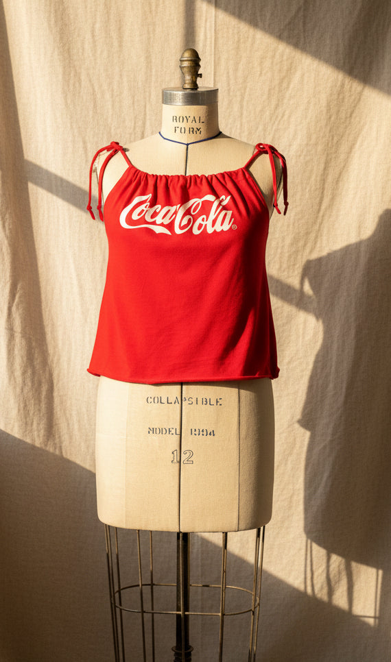 Red tank top with Coca-Cola logo on a mannequin against a beige curtain.