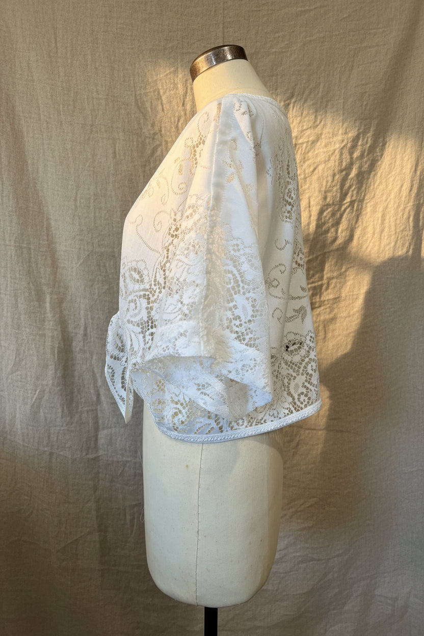 A white lace shawl with embroidered floral patterns draped over a cream-colored dress form mannequin in an indoor room setting.