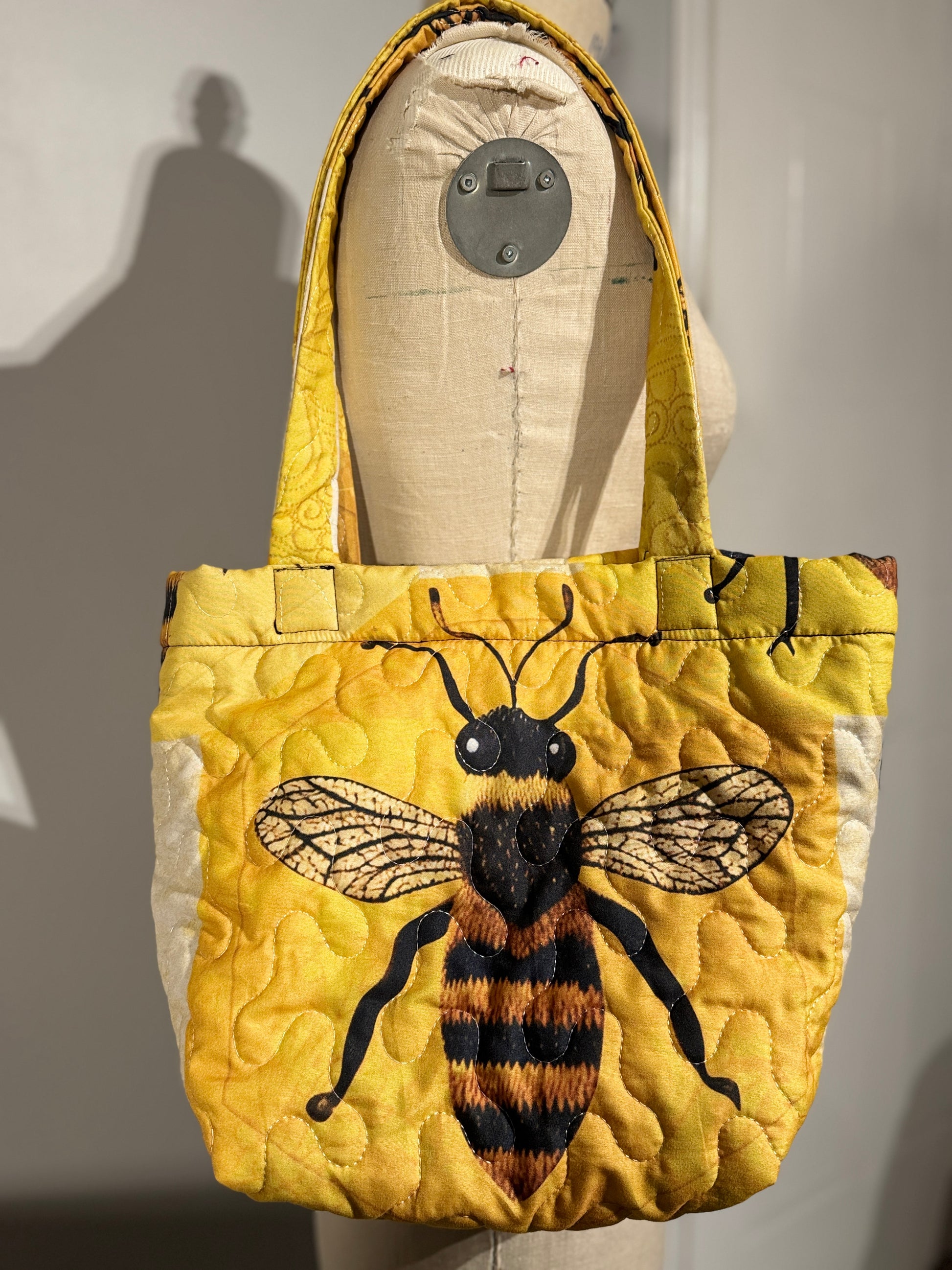 Yellow quilted bag with a bee design on a mannequin