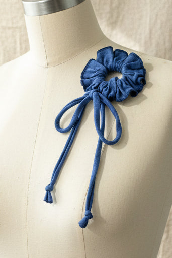 A blue scrunchie with long tie strings, displayed on a beige fabric dress form.