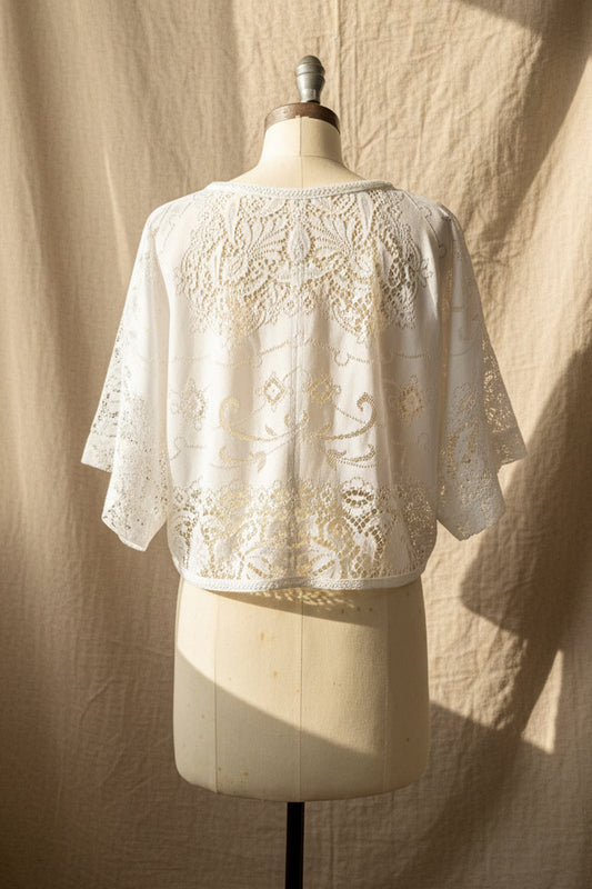 A white lace-trimmed knit top displayed on a cream dress form mannequin, showing the back view with ornate floral lace embroidery and 3/4 sleeves in an indoor room setting.