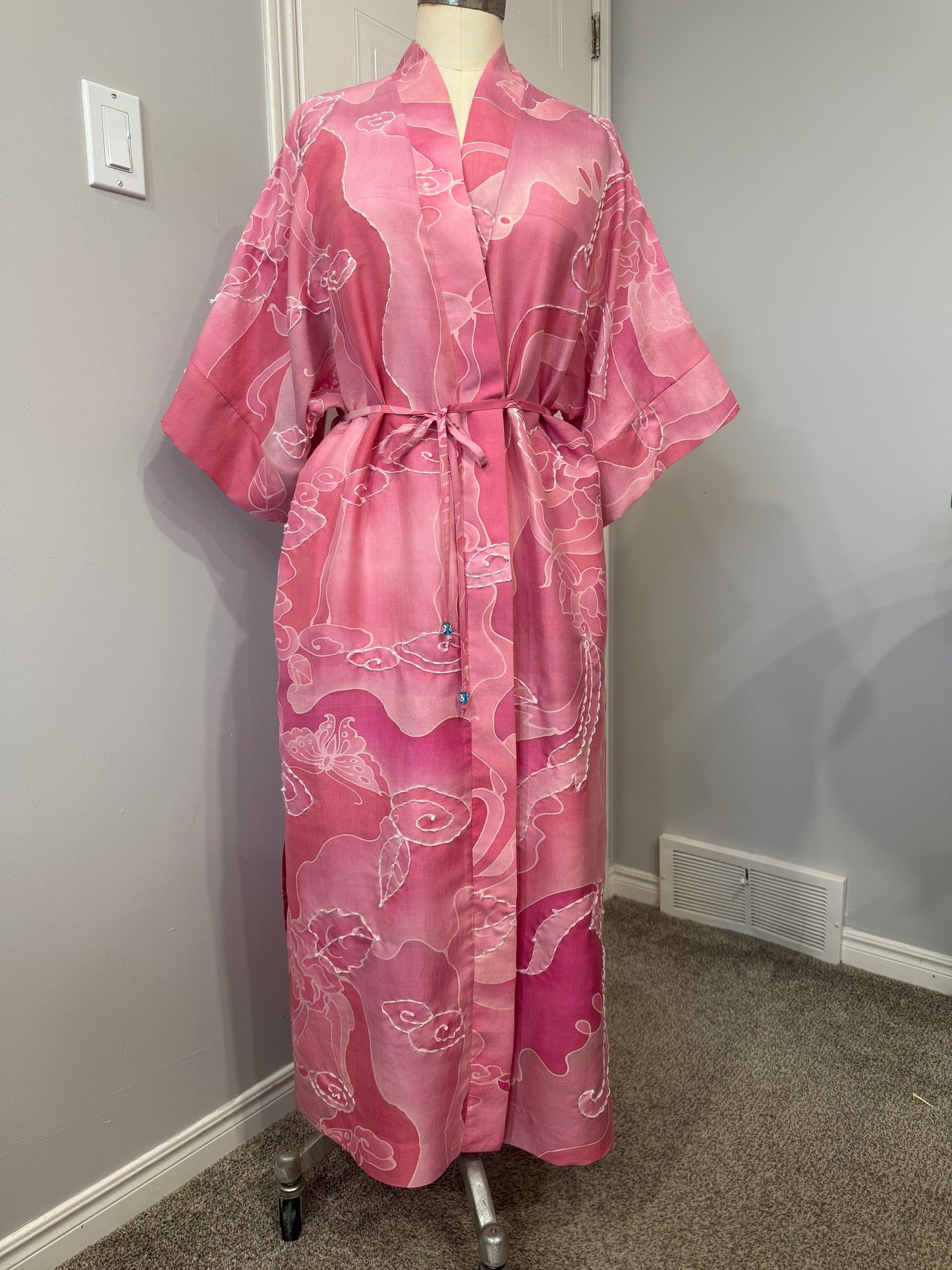 Pink dress with floral pattern on a mannequin against a white wall.