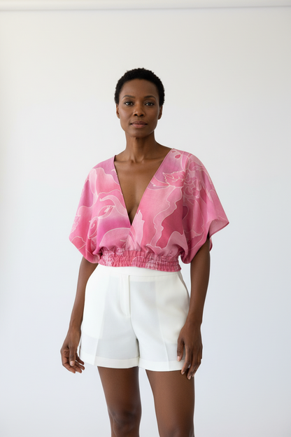 Person wearing a pink blouse with white shorts on a plain background