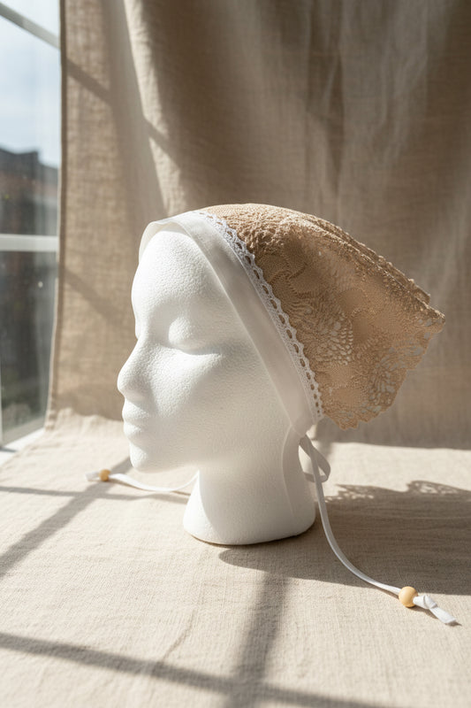 Mannequin head wearing a beige head scarf with lace details against a neutral background