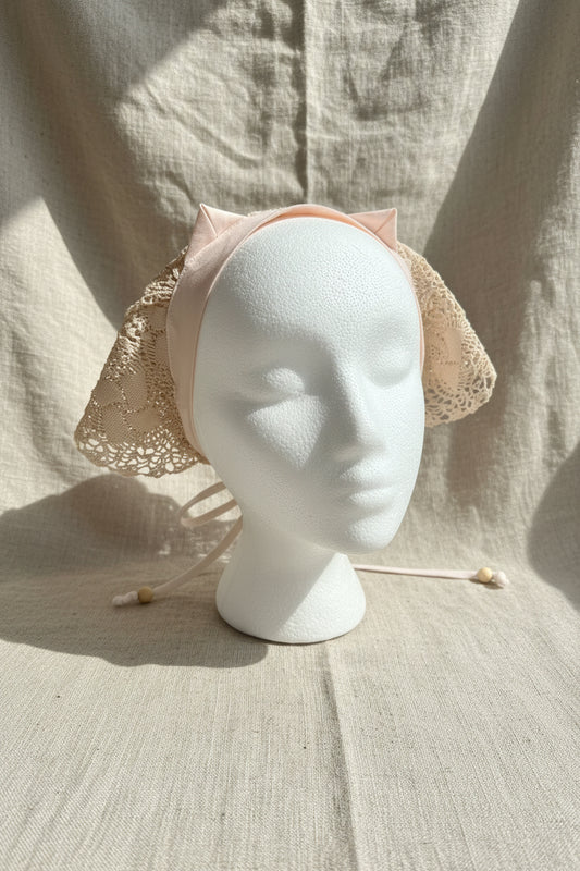 Mannequin head wearing a beige lace bonnet on a neutral background