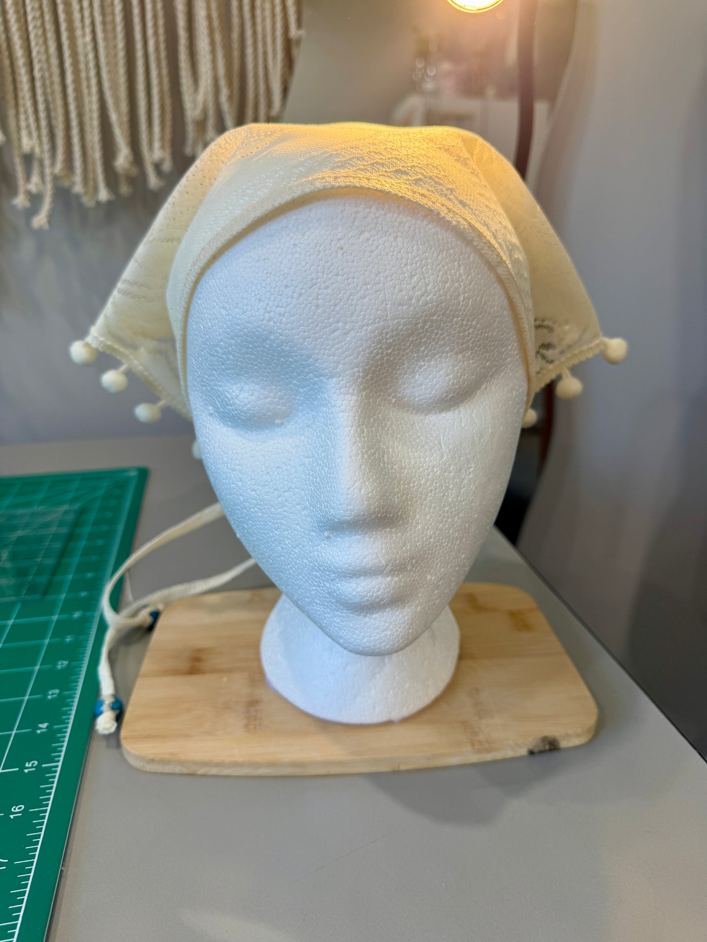 Mannequin head with a beige headscarf on a wooden stand, with a blurred background.