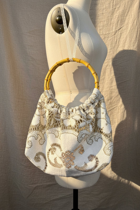 Decorative handbag with floral embroidery and bamboo handle on a mannequin against a neutral background