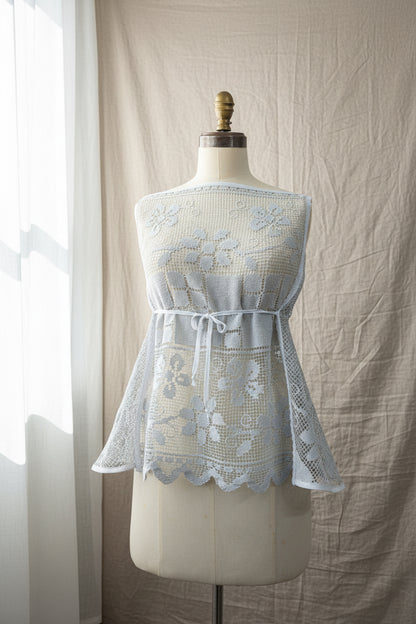 Blue-grey lace dress on a mannequin against a beige curtain background