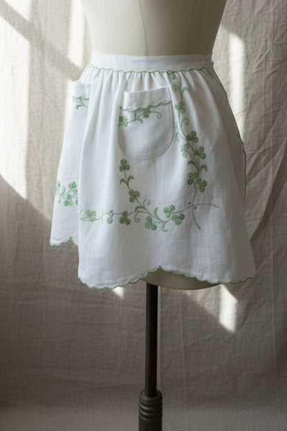 White apron with green embroidery on a mannequin against a neutral background