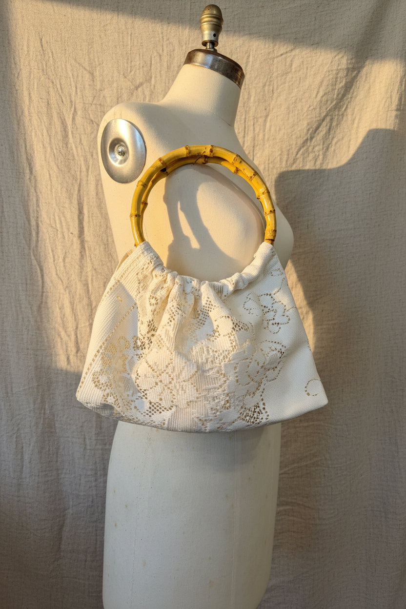 Mannequin holding an ivory lace purse with a bamboo handles against a beige curtain background